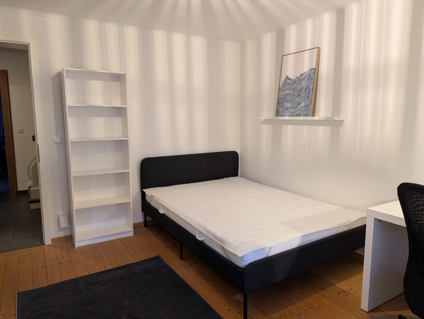Zimmer EG links Helles Zimmer mit einem Bett, einem Regal und einem Schreibtisch.