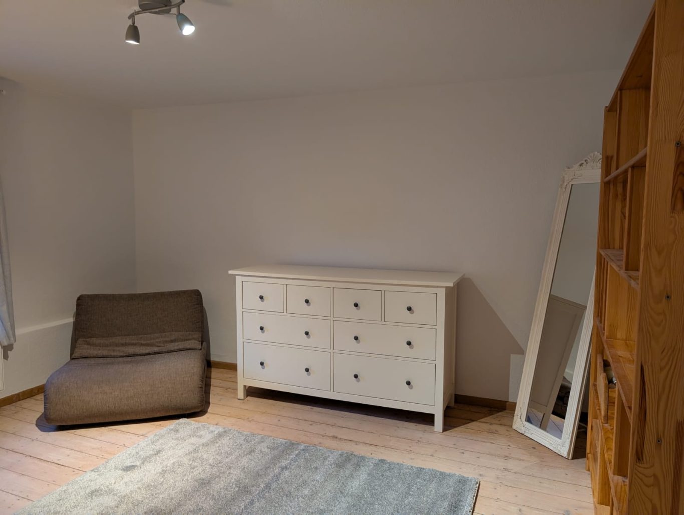 Zimmer 2 OG rechts Ein heller Raum mit einem weißen Kommode, einem gemütlichen Sessel und einem großen Spiegel.