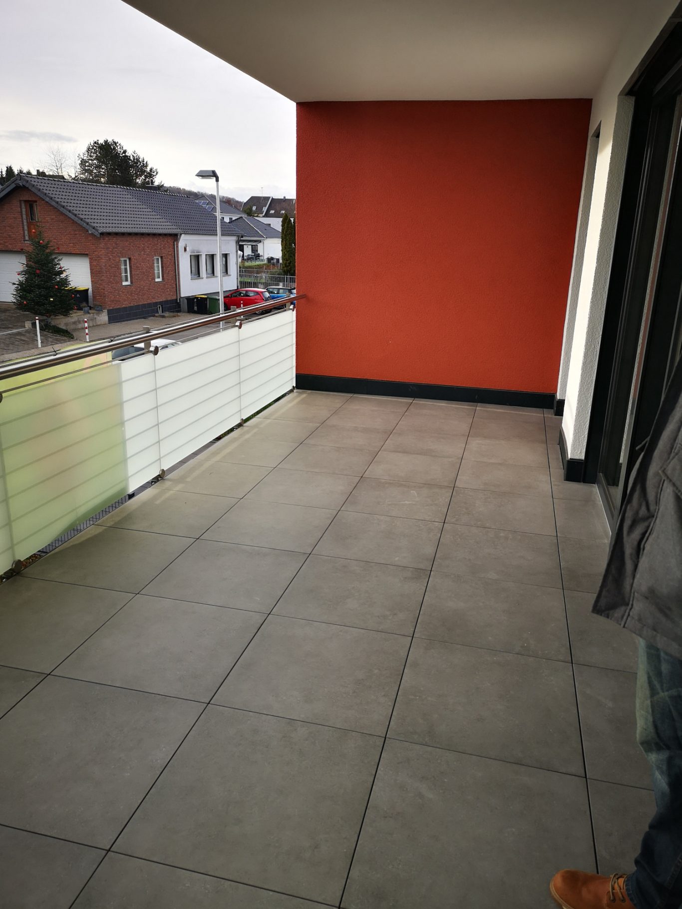 Loggia Balkon mit grauen Fliesen und roter Wand im Hintergrund, unmöbliert und leer.