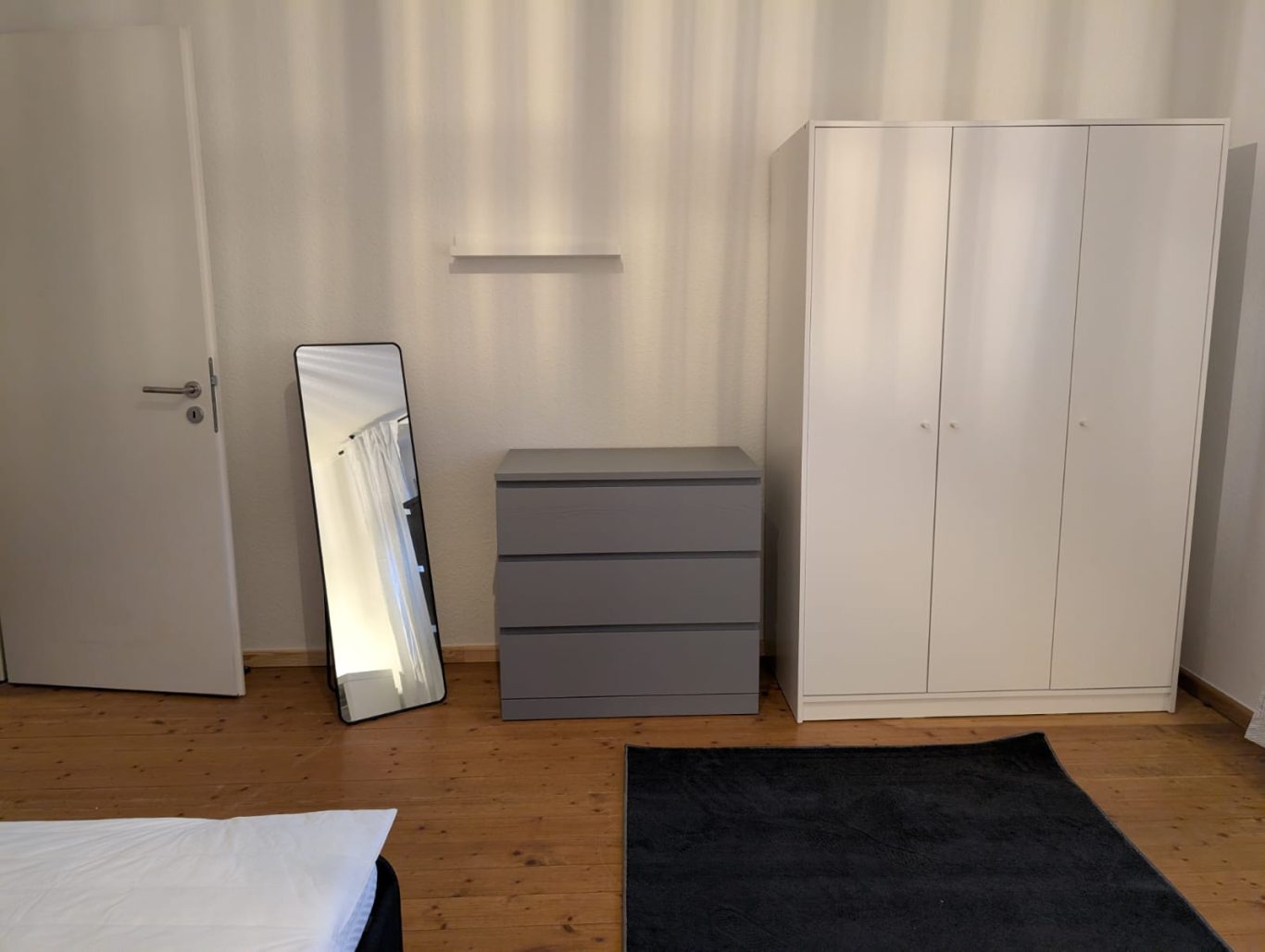 Zimmer EG rechts Helles Zimmer mit einem Kleiderschrank, Kommode, Spiegel und Teppich.