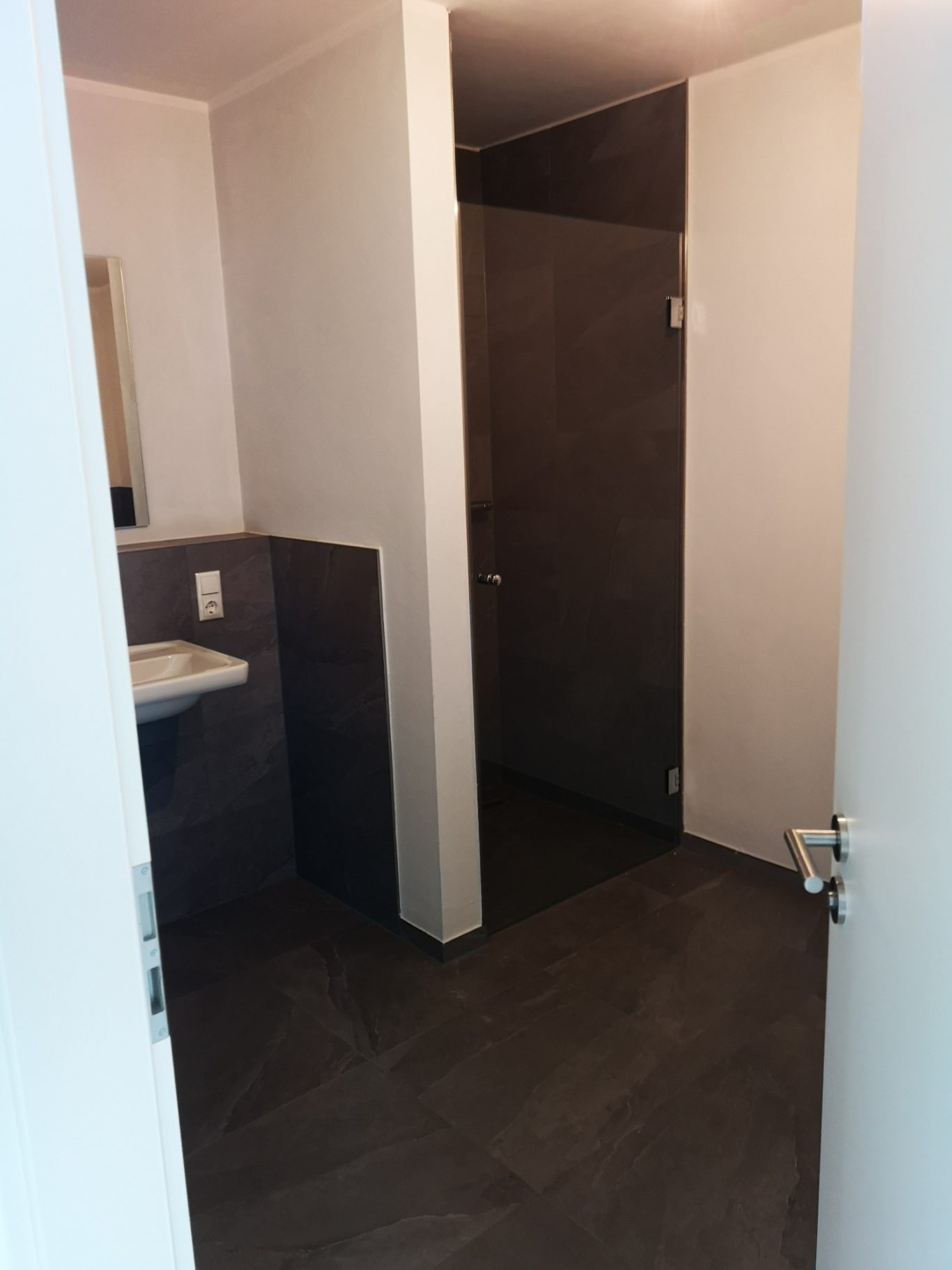 Bad links mit Waschbecken und Dusche Blick in ein modernes, neutrales Badezimmer mit Waschbecken und Tür.
