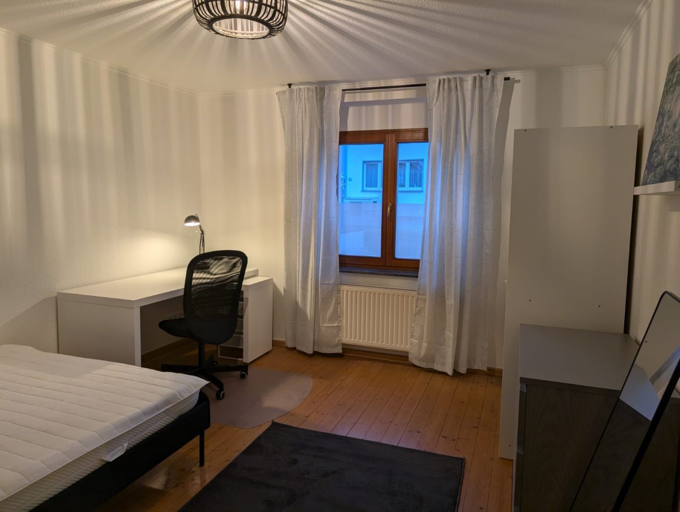 Zimmer EG links Helles, einfaches Zimmer mit Bett, Schreibtisch, Stuhl und Fenster.