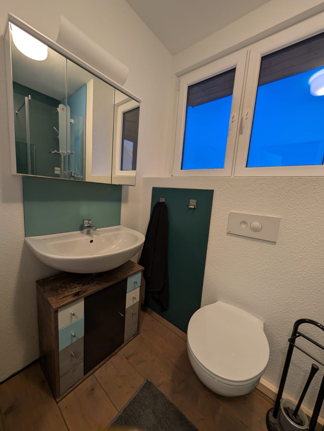 kleines Bad Dachgeschoss links Modernes Badezimmer mit Waschbecken, Wandtoilette und großen Fenstern.