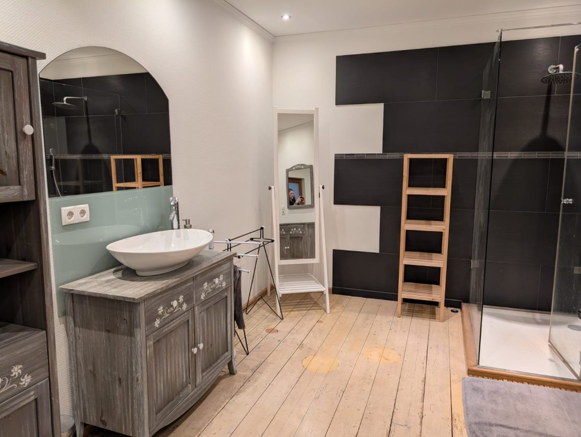großes Bad Waschbecken Modernes Badezimmer mit Dusche, Waschbecken und Holzboden. Schlichte Möbel und helle Wände.