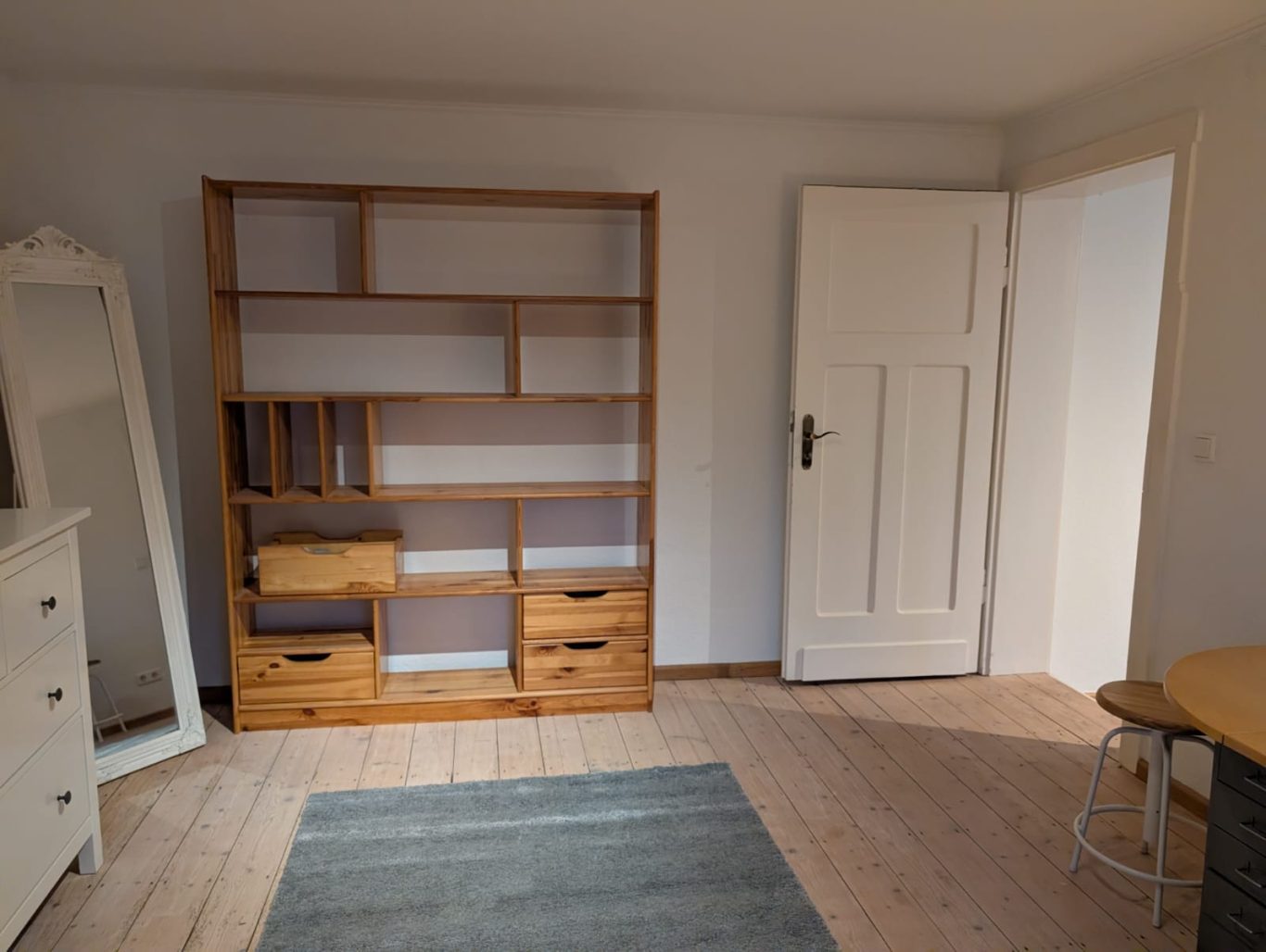 Zimmer 2 OG rechts Helles Zimmer mit einem Holzregal, einem Tisch und einer Tür.