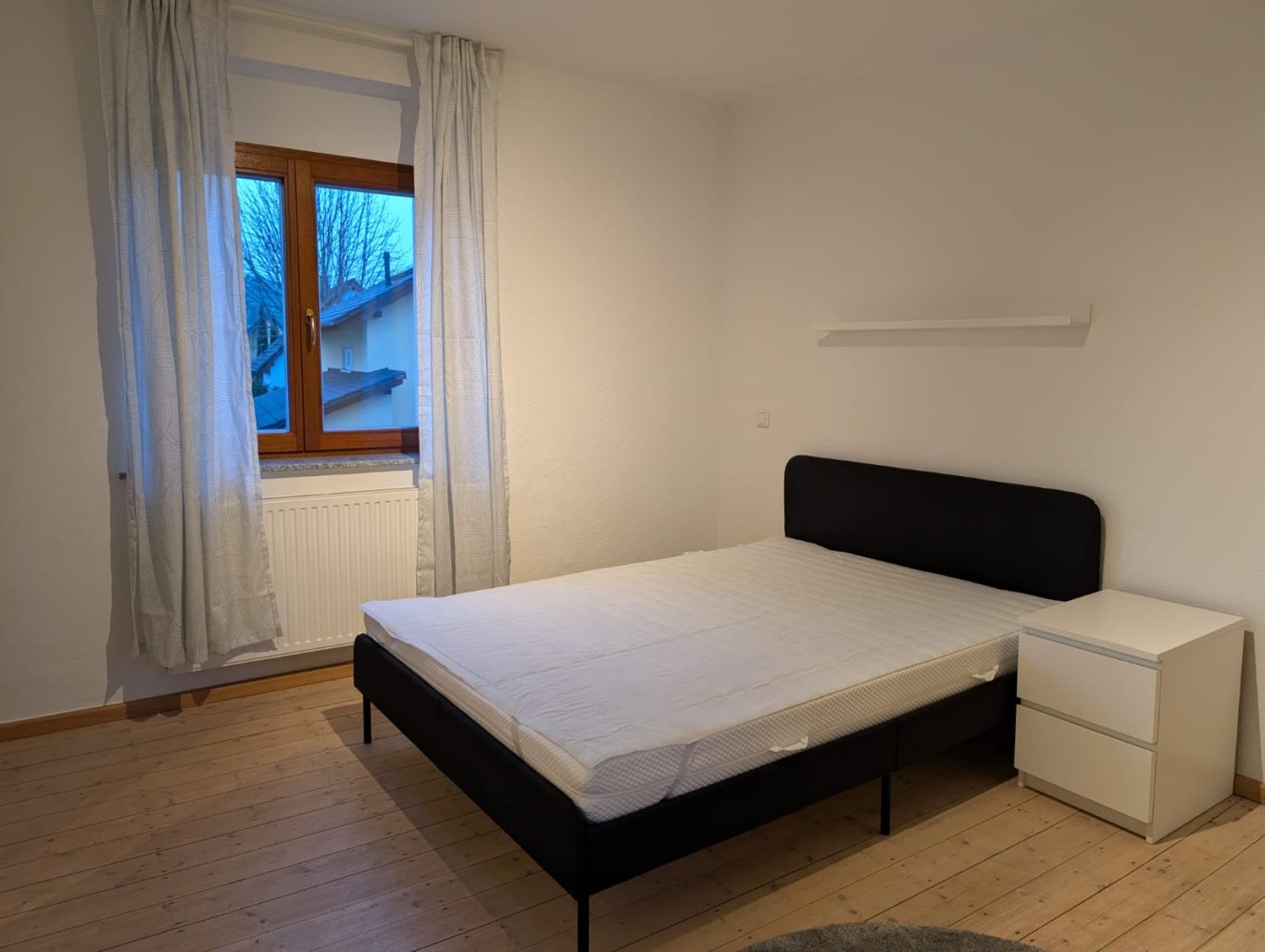 Zimmer 1 OG rechts Hellbezeichneter Raum mit einem Bett und einem Nachttisch neben einem Fenster.